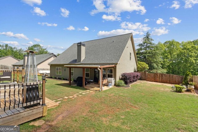 rear view of house with a chimney, a patio area, a shingled roof, a lawn, and a fenced backyard