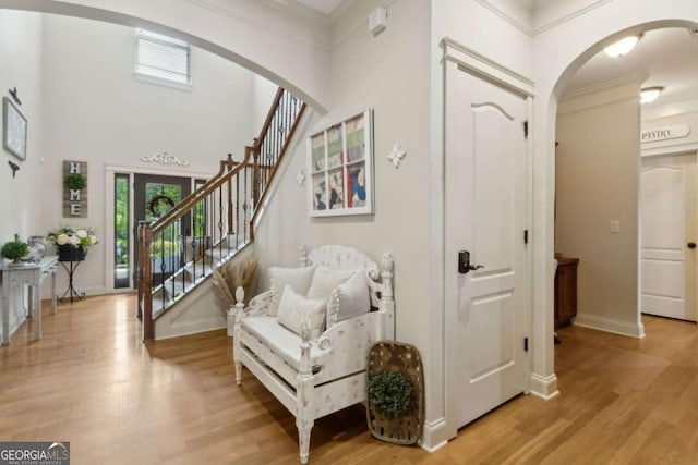 foyer featuring crown molding, light wood-style floors, baseboards, arched walkways, and stairs