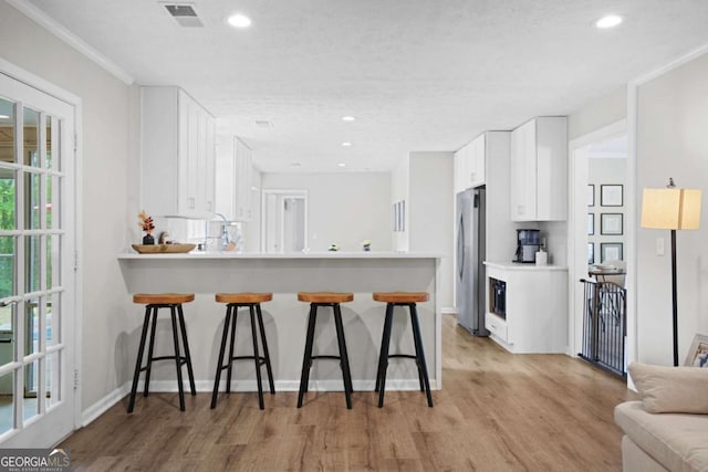 kitchen featuring visible vents, freestanding refrigerator, a breakfast bar area, white cabinetry, and light wood-style flooring