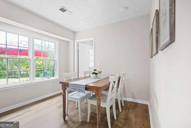 dining space with baseboards, a textured ceiling, wood finished floors, and visible vents