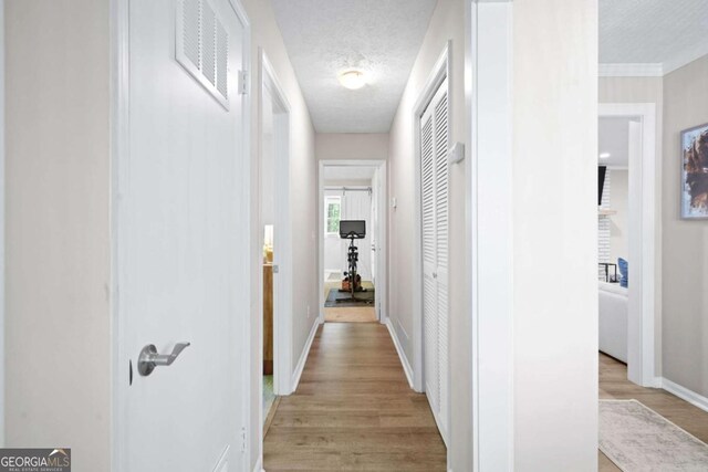 hallway with visible vents, a textured ceiling, light wood-style floors, and baseboards