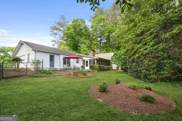 back of house featuring a chimney, a sunroom, fence, a yard, and an attached garage