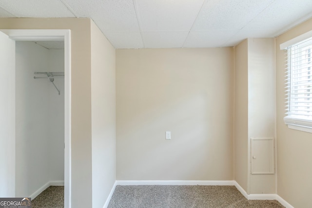 unfurnished bedroom featuring baseboards, a spacious closet, a drop ceiling, and carpet
