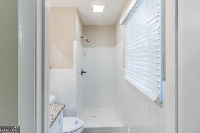 full bath with vanity, toilet, a wainscoted wall, tile walls, and a stall shower