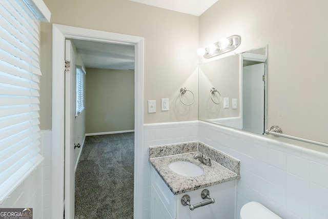 half bath featuring toilet, tile walls, wainscoting, and vanity