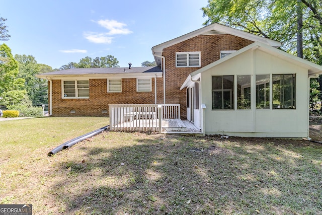 rear view of house with a sunroom, a yard, brick siding, and a deck