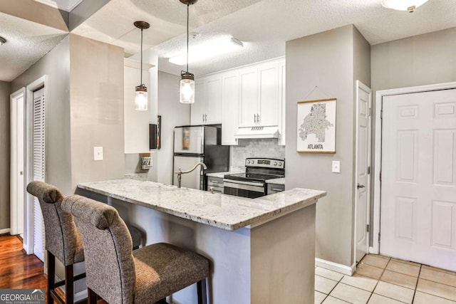 kitchen with a peninsula, a textured ceiling, under cabinet range hood, white cabinets, and appliances with stainless steel finishes