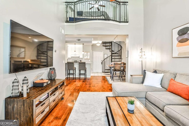 living room with a ceiling fan, stairway, a towering ceiling, and wood finished floors
