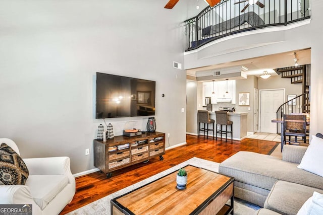 living area featuring baseboards, visible vents, ceiling fan, wood finished floors, and stairway