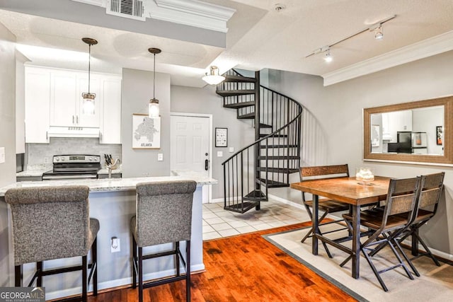 kitchen with under cabinet range hood, visible vents, a kitchen bar, white cabinetry, and stainless steel range with electric cooktop