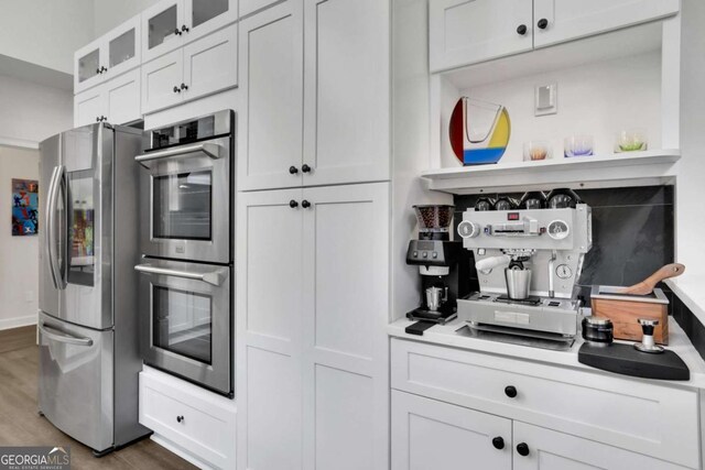kitchen featuring appliances with stainless steel finishes, wood finished floors, white cabinetry, and glass insert cabinets