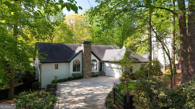 view of front of house featuring a chimney, roof with shingles, driveway, and an attached garage