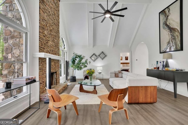 living area with beam ceiling, a fireplace, wood finished floors, a ceiling fan, and high vaulted ceiling