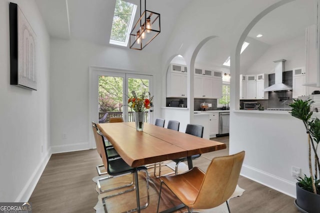 dining space with lofted ceiling, wood finished floors, baseboards, and arched walkways