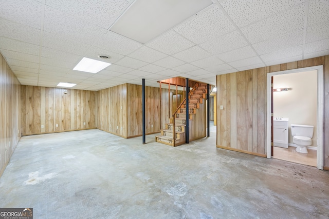 finished basement featuring stairs, wooden walls, and a drop ceiling