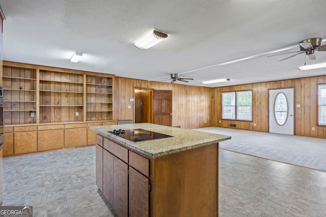 kitchen featuring wooden walls, a center island, ceiling fan, and black electric stovetop