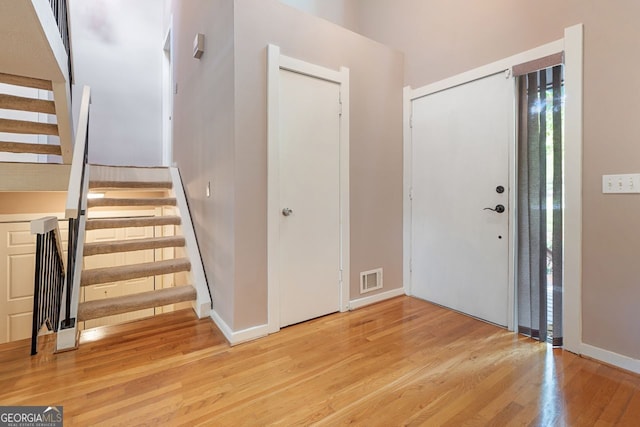 entryway featuring baseboards, visible vents, light wood-type flooring, and stairs