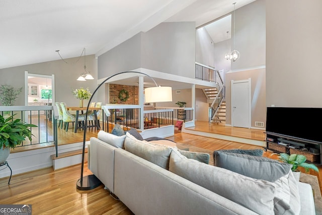 living area with visible vents, wood finished floors, stairway, high vaulted ceiling, and a chandelier