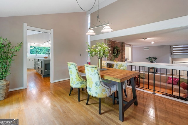dining room featuring baseboards, vaulted ceiling, light wood finished floors, and visible vents