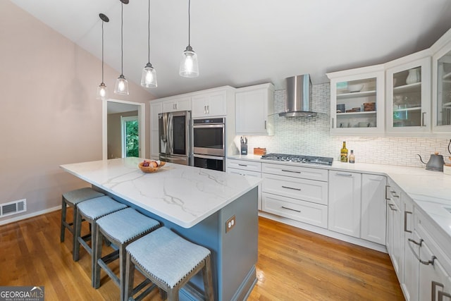 kitchen with wall chimney range hood, a center island, stainless steel appliances, backsplash, and visible vents