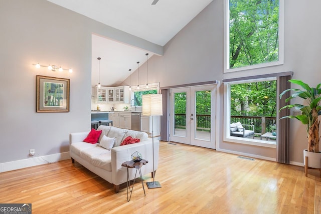 living room featuring a ceiling fan, visible vents, high vaulted ceiling, baseboards, and light wood finished floors