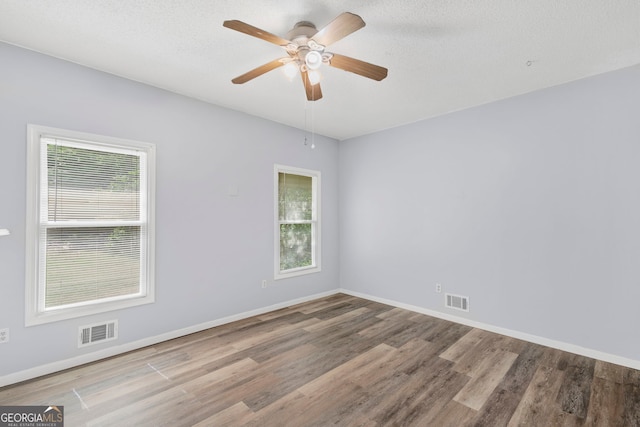 unfurnished room featuring visible vents, wood finished floors, and a wealth of natural light