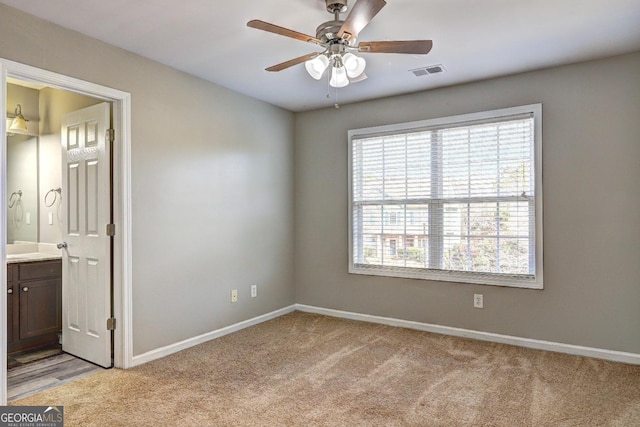 unfurnished bedroom featuring visible vents, ceiling fan, baseboards, light carpet, and ensuite bath