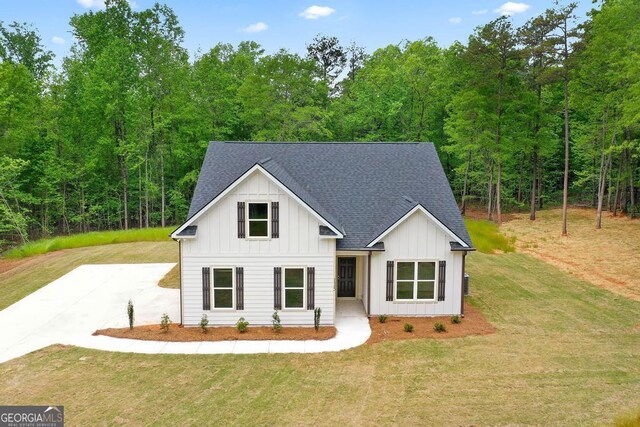 modern farmhouse featuring board and batten siding, a front yard, concrete driveway, and roof with shingles