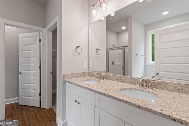 full bathroom featuring double vanity, wood finished floors, a stall shower, and a sink