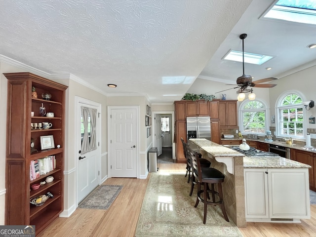 4614 Capers Xing W, Peachtree Corners, GA 30092 - kitchen with light wood-style floors, brown cabinets, light stone counters, a skylight, and stainless steel appliances