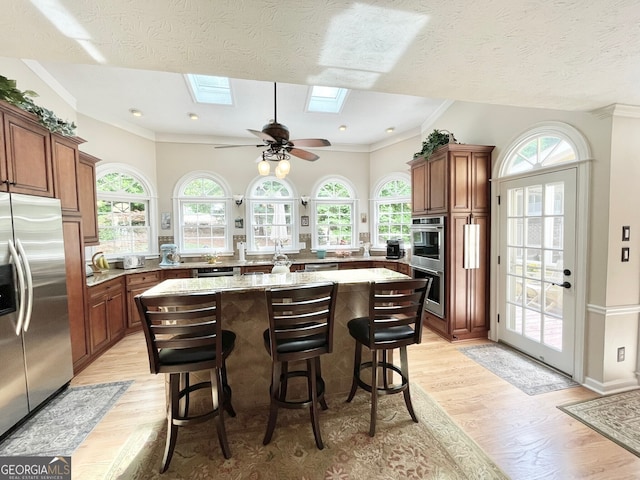 4614 Capers Xing W, Peachtree Corners, GA 30092 - kitchen featuring light wood-style floors, stainless steel appliances, a kitchen bar, a kitchen island, and a skylight