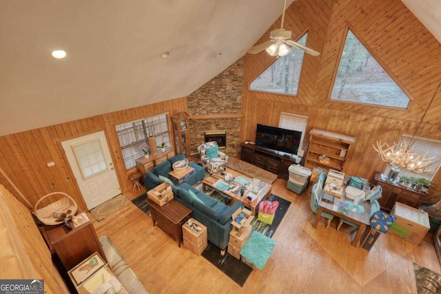 living area with high vaulted ceiling, wood finished floors, ceiling fan with notable chandelier, and wooden walls