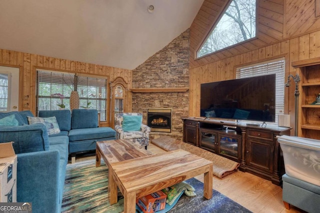 living room featuring high vaulted ceiling, wood finished floors, a stone fireplace, and wood walls