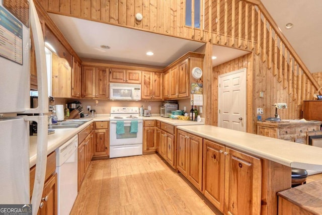 kitchen featuring brown cabinets, light wood-style floors, white appliances, a peninsula, and light countertops