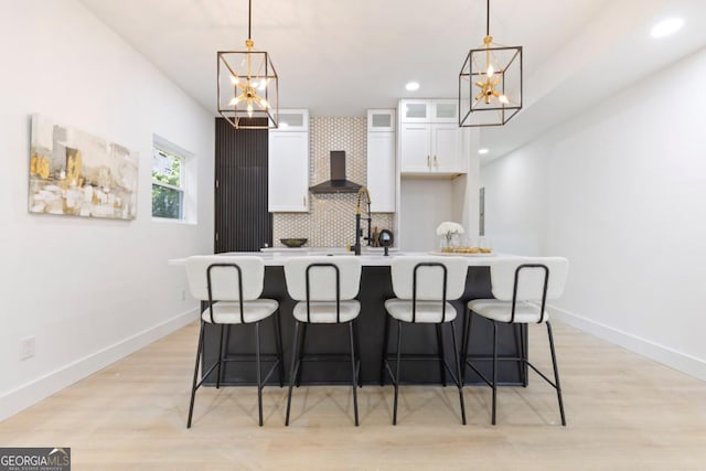 kitchen featuring wall chimney range hood, white cabinets, an island with sink, and a notable chandelier
