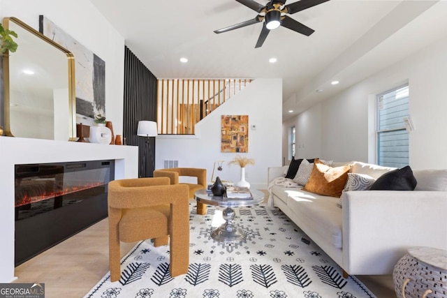living room with light wood-type flooring, recessed lighting, a glass covered fireplace, and ceiling fan