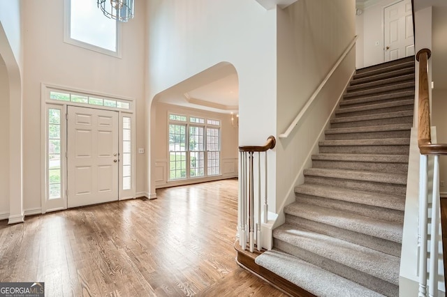 entryway featuring arched walkways, baseboards, wood finished floors, a towering ceiling, and stairway