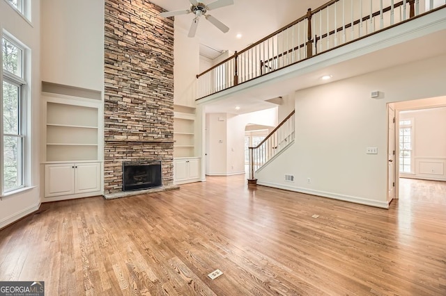 unfurnished living room with a towering ceiling, wood finished floors, a fireplace, ceiling fan, and built in shelves