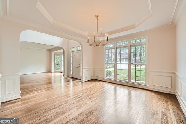 empty room featuring an inviting chandelier, a raised ceiling, a decorative wall, light wood-style floors, and arched walkways