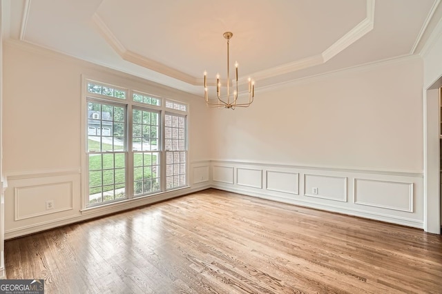 spare room featuring a wainscoted wall, a tray ceiling, wood finished floors, and a chandelier