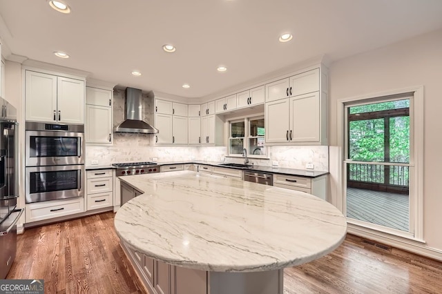 kitchen with visible vents, wood finished floors, a sink, stainless steel appliances, and wall chimney exhaust hood