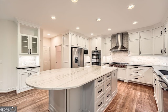 kitchen featuring light stone countertops, wall chimney range hood, a center island, tasteful backsplash, and stainless steel appliances