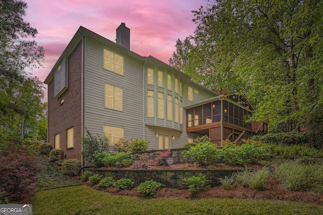 back of property at dusk with a chimney and a sunroom