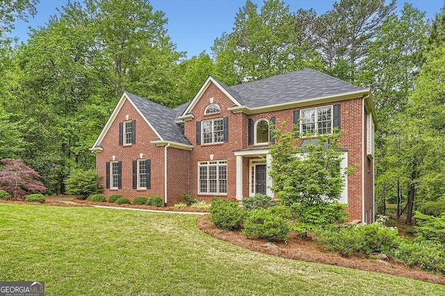 colonial-style house with brick siding, a front lawn, and roof with shingles