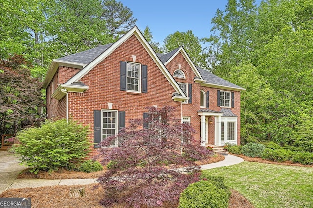colonial home with brick siding, a front yard, and roof with shingles