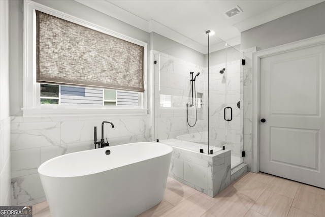 full bath with a freestanding bath, a marble finish shower, tile walls, and visible vents