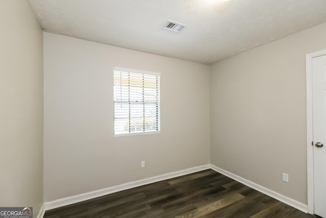 empty room with dark wood-style floors, visible vents, and baseboards