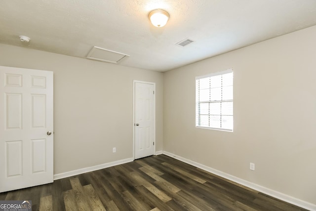 unfurnished room featuring attic access, dark wood-style floors, visible vents, and baseboards