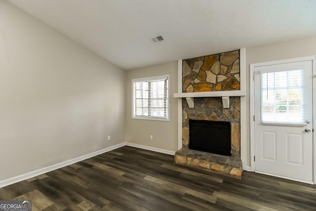 unfurnished living room with visible vents, a stone fireplace, baseboards, and dark wood-type flooring