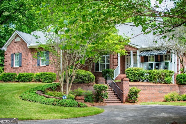 view of front of home featuring a porch, brick siding, stairs, and a front yard